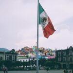 Colorful cityscape of Toluca with large Mexican flag in the foreground, vibrant buildings in the backdrop.